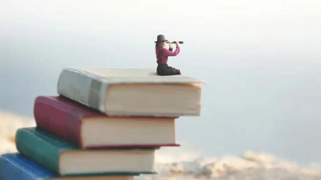 imagem de mulher sobre torre de livros mostrando benefícios da leitura