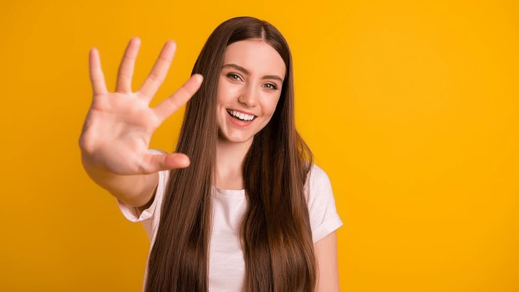 Mulher fazendo o número cinco com a mão em fundo amarelo